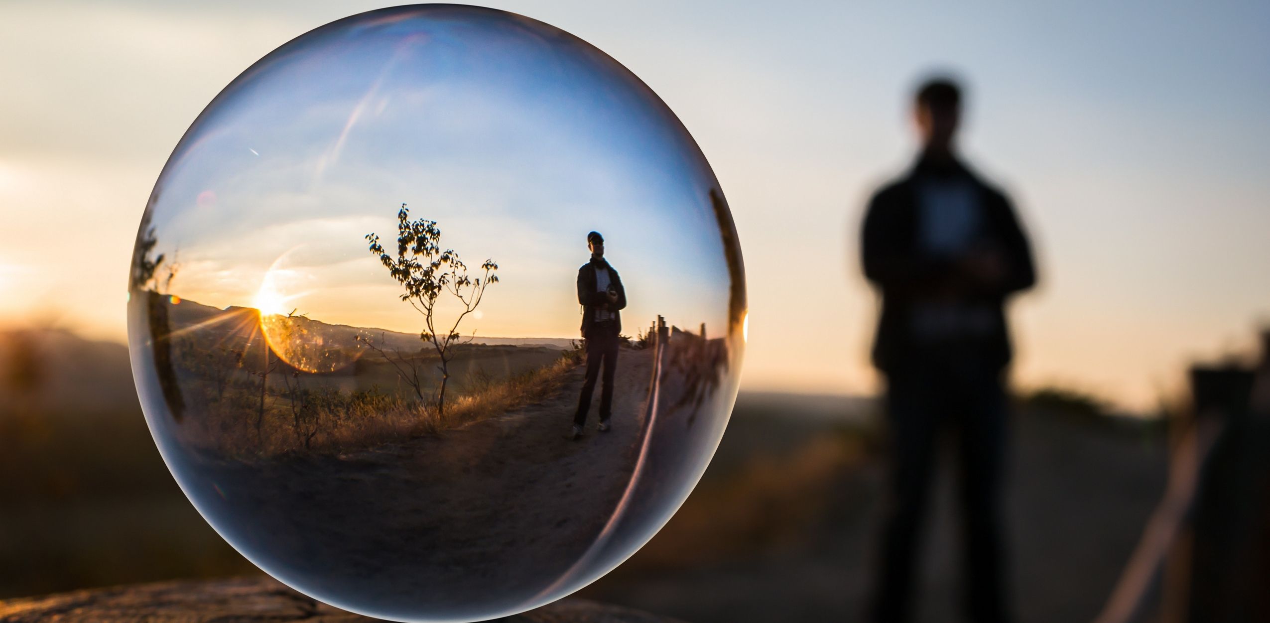 A sunset horizon and a person standing fairly close by, all reflected through a bubble up-close.